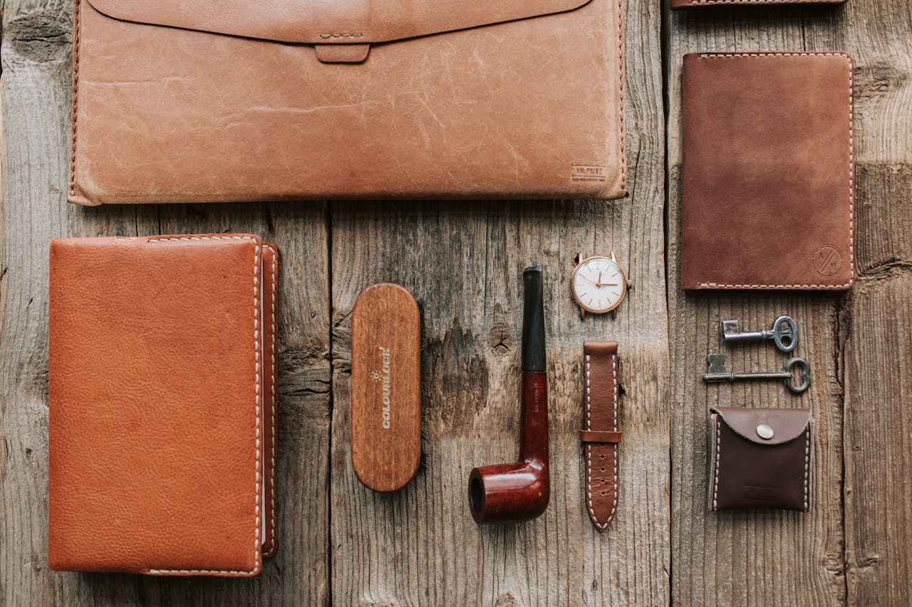 Elegant composition of leather goods and pipe on rustic wooden surface for a classic vibe.
